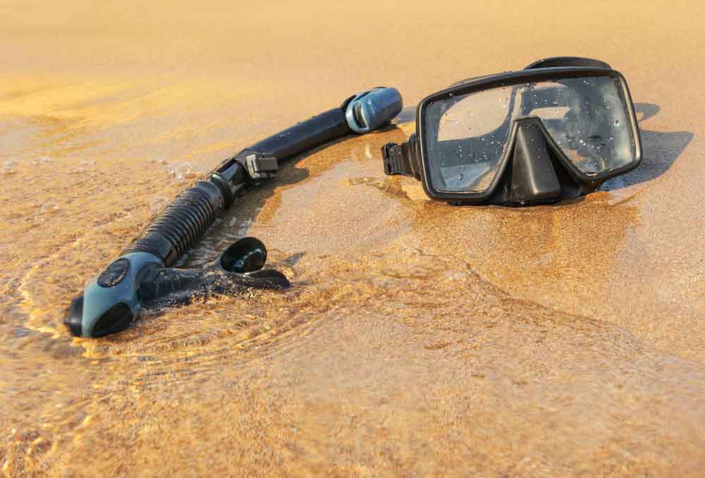 52506452_sun-shining-to-black-snorkel-and-diving-mask-on-wet-beach-sand-washed-by-sea a-diving-equipment-with-regulators-and-tools-for-checking-barrels.